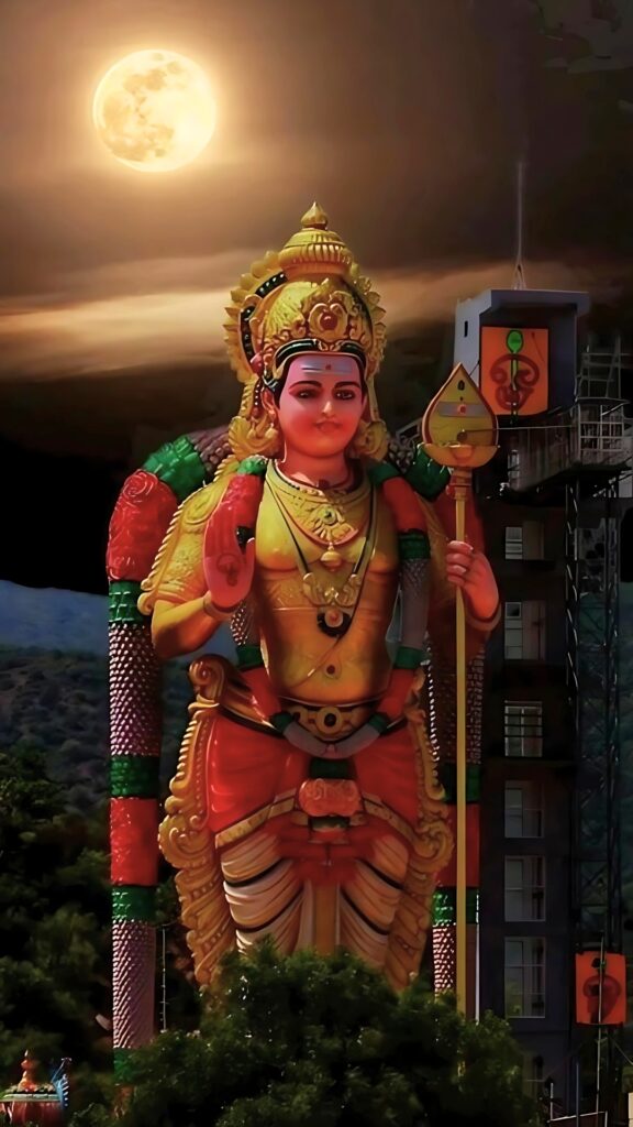 Devotional HD image of Lord Murugan statue under full moonlight, depicting the Hindu god Kartikeya with his divine Vel in vibrant attire.