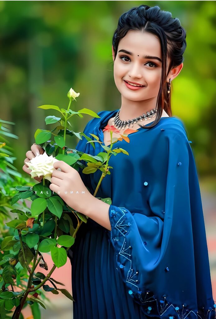 Beautiful Indian girl in a blue ethnic dress smiling and holding a white rose outdoors in a garden