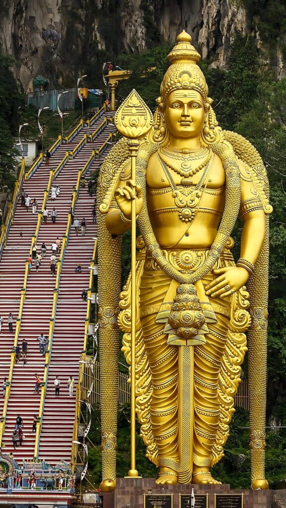 Majestic golden statue of Lord Kartikeya (Murugan) at Thiruchendur with temple steps in background, representing Hindu devotion and pilgrimage