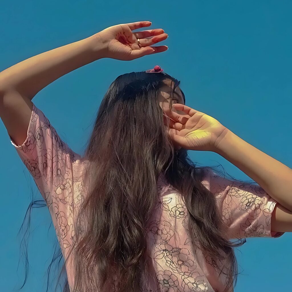 Hidden face aesthetic photo of a girl with long hair in a pink floral shirt under clear blue sky – moody sunlight aesthetic for girls