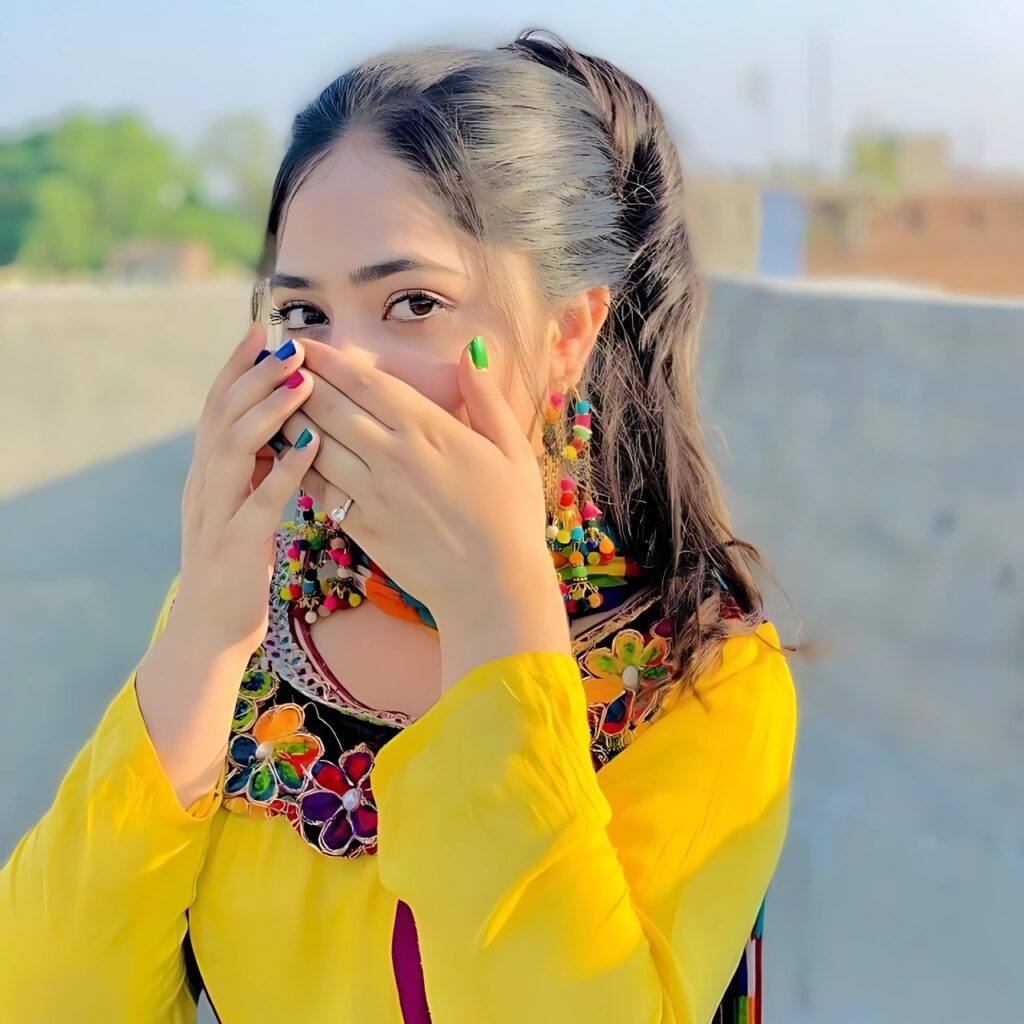 Young Indian girl in colorful traditional dress covering her mouth with hands, vibrant nail colors, rooftop background