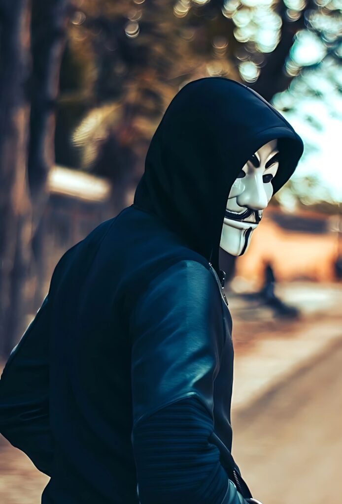Boy in a hoodie wearing a Guy Fawkes mask, looking back on an empty street with a somber vibe