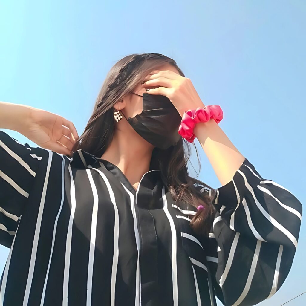 Girl hiding face with hand wearing black mask and striped shirt – aesthetic Instagram photo under blue sky