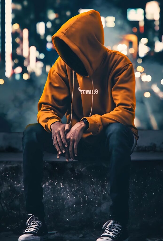 Single boy wearing orange hoodie and black jeans, sitting alone at night with city lights in the background, perfect moody profile pic.