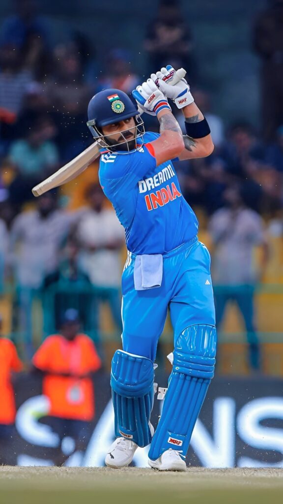 Virat Kohli playing a textbook lofted shot in Team India’s blue jersey – Dream11 India kit with MRF bat, stadium action in the background.