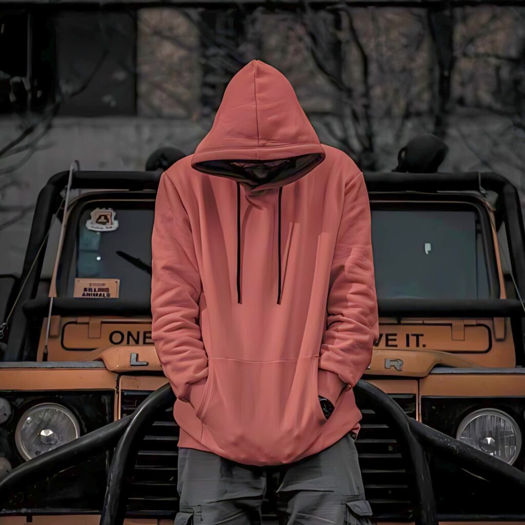 Boy in red hoodie with head down, standing in front of a rugged vehicle, giving off a strong, mysterious attitude vibe – ideal for WhatsApp DP