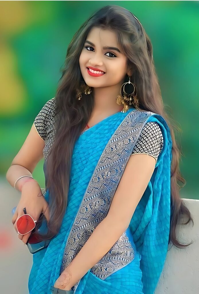 नीली साड़ी में मुस्कुराती हुई सुंदर भारतीय लड़की, पारंपरिक पहनावे में, बैकग्राउंड में हरियाली के साथ।
