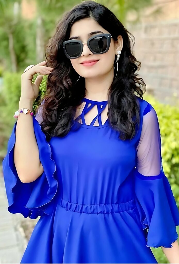 ब्लू वेस्टर्न ड्रेस में स्टाइलिश भारतीय लड़की, बड़े काले सनग्लासेस और खुले घुंघराले बालों के साथ।
