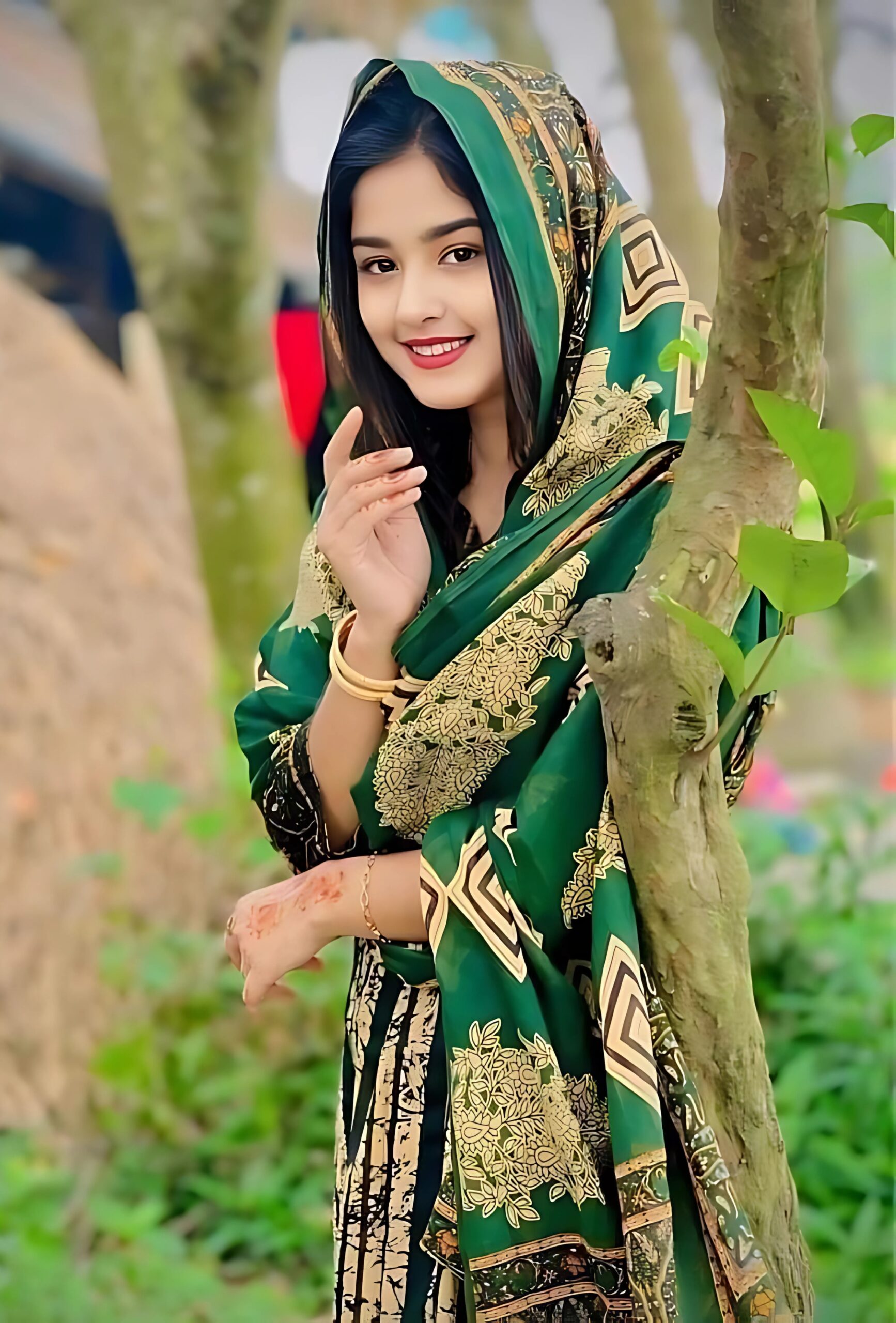 Muslim girl in green and gold traditional attire smiling in a natural outdoor setting