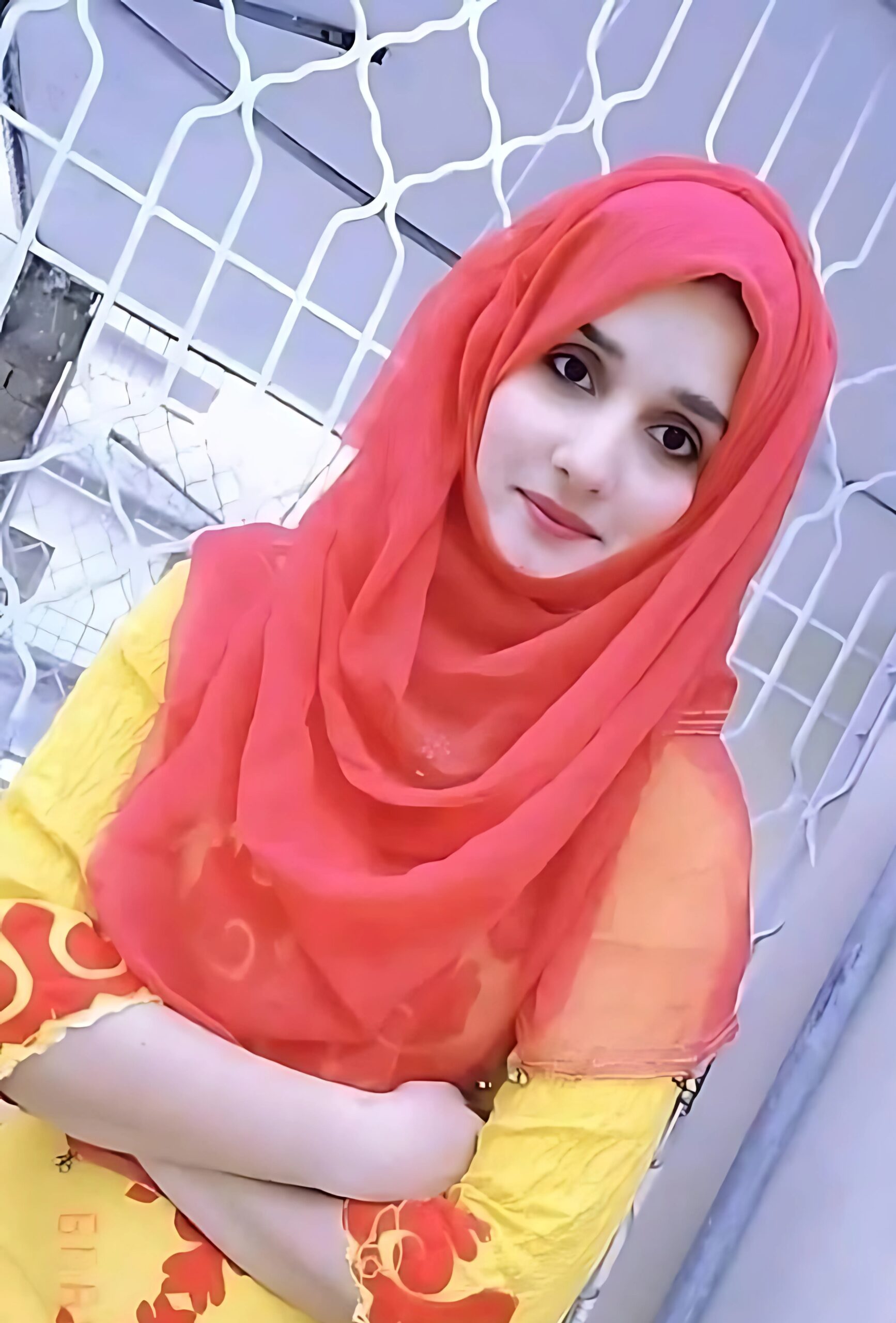 Muslim ladki in red dupatta and yellow embroidered dress posing confidently in front of a gate