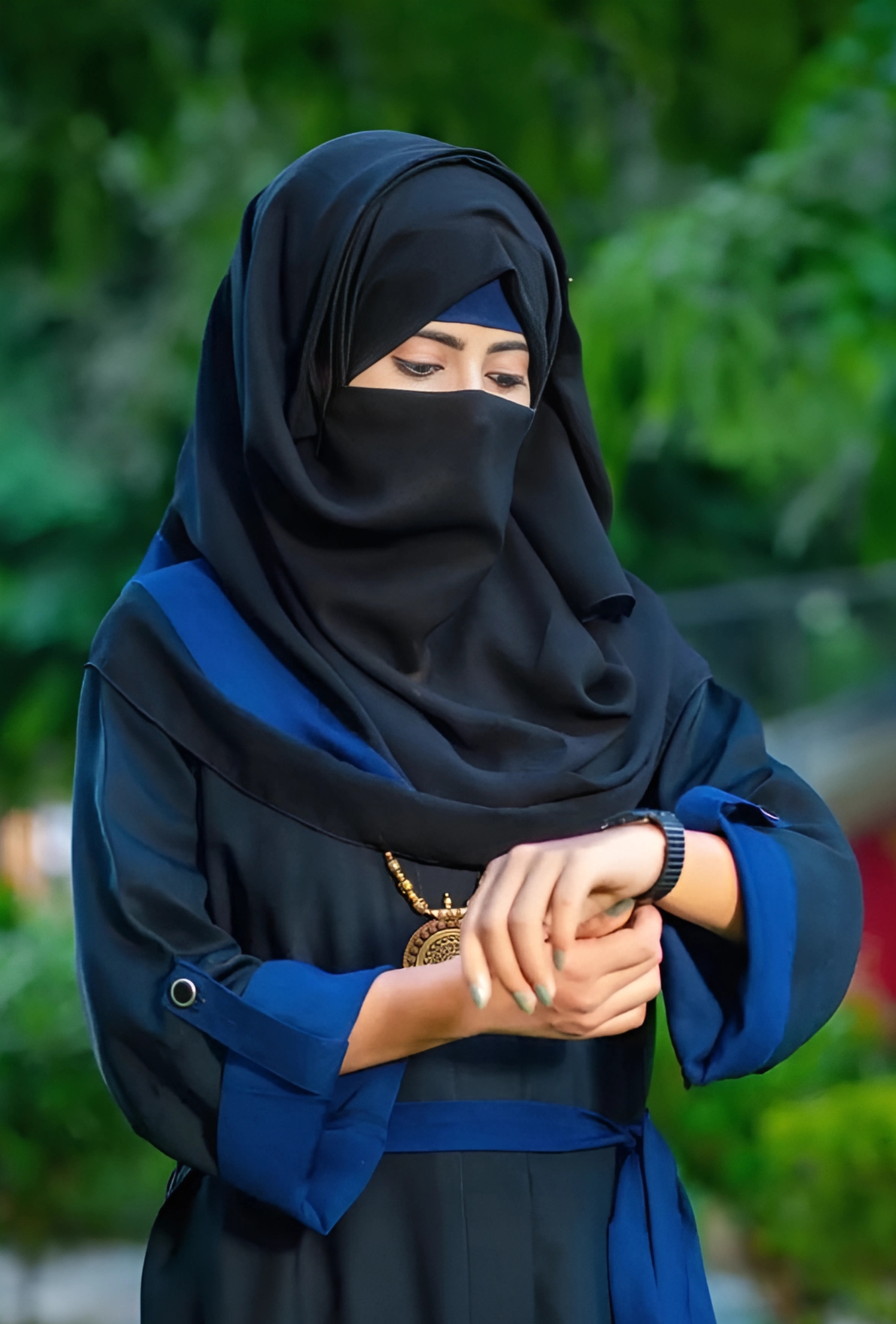 Modest Muslim girl in black and blue abaya looking at her watch – beautiful hijab girl DP.