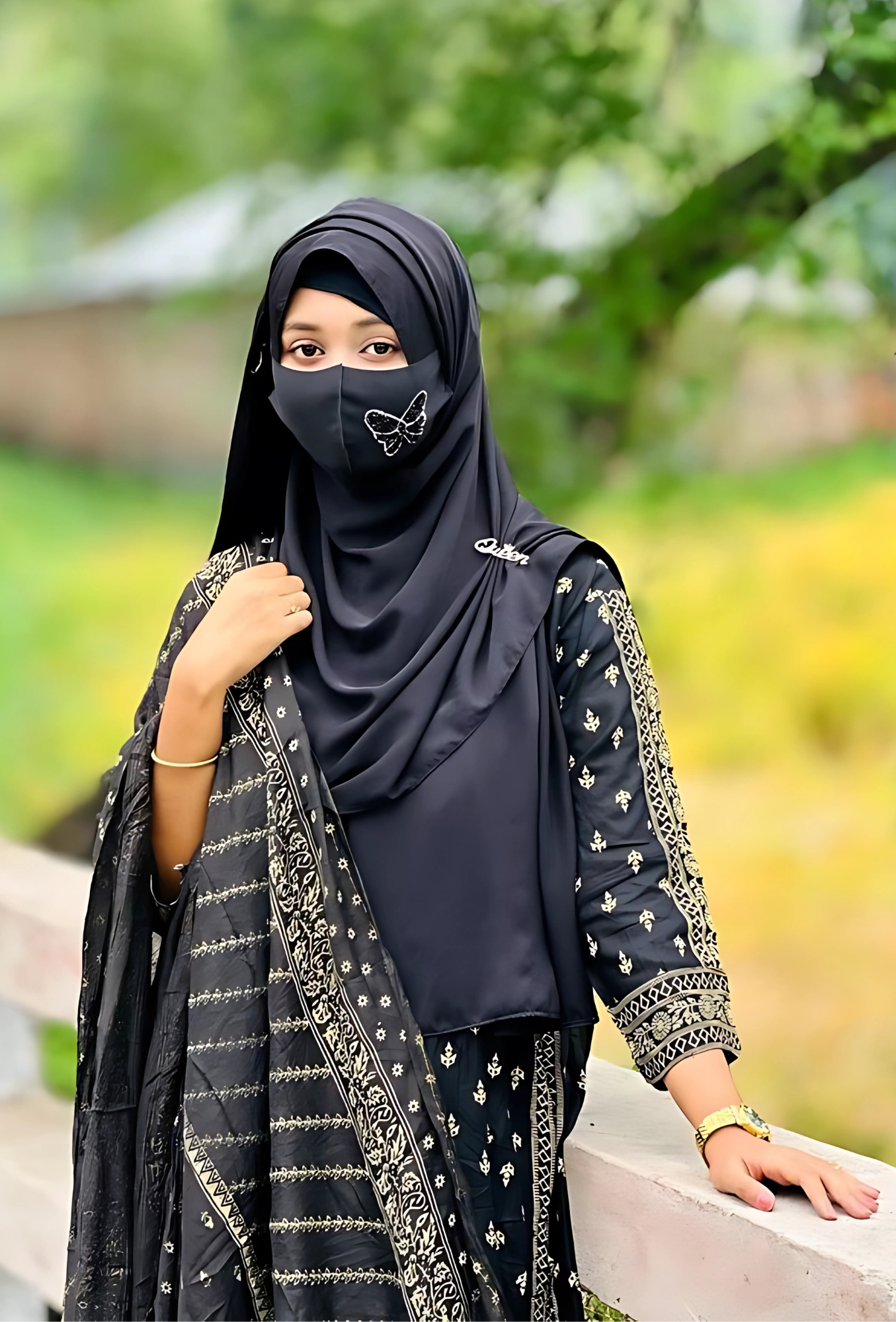 Beautiful Muslim hijab girl standing outdoors in traditional black dress with elegant embroidery, wearing a butterfly mask and posing gracefully near a bridge, perfect for hijab girl with boy dp.