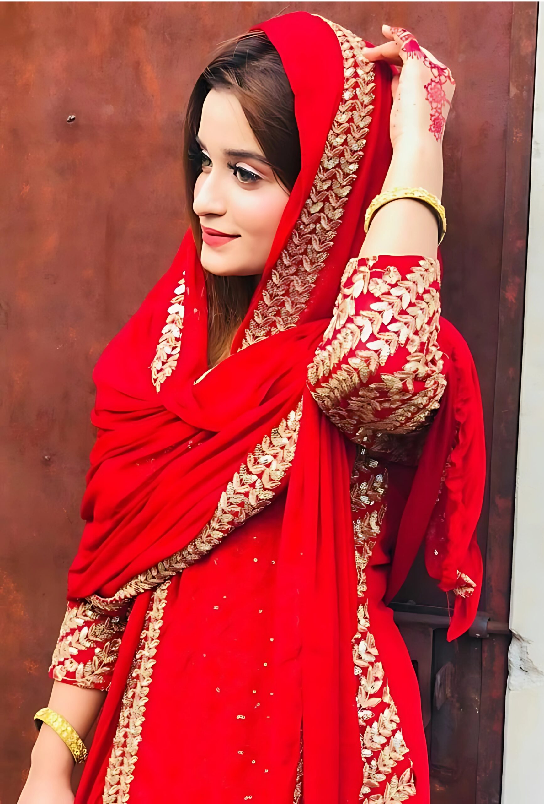 Muslim girl in traditional red dress with golden embroidery, standing gracefully with henna on hand