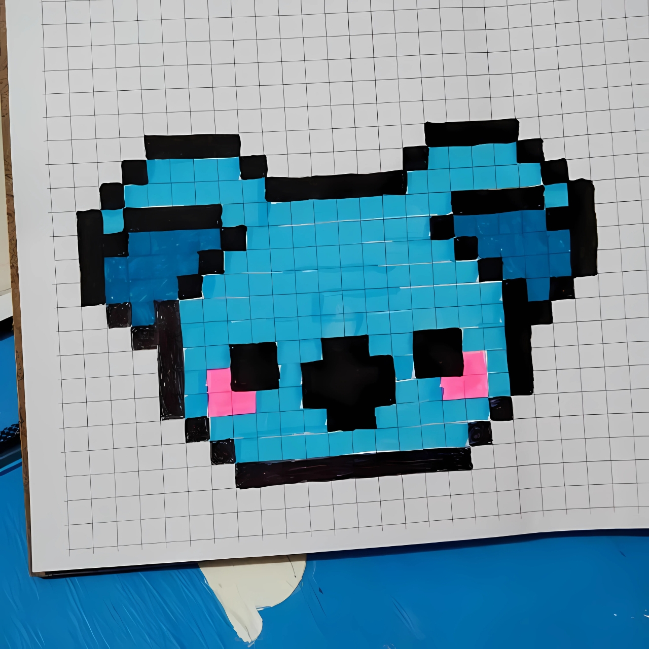 Dibujo pixelado kawaii de un koala azul con mejillas rosadas sobre papel cuadriculado.