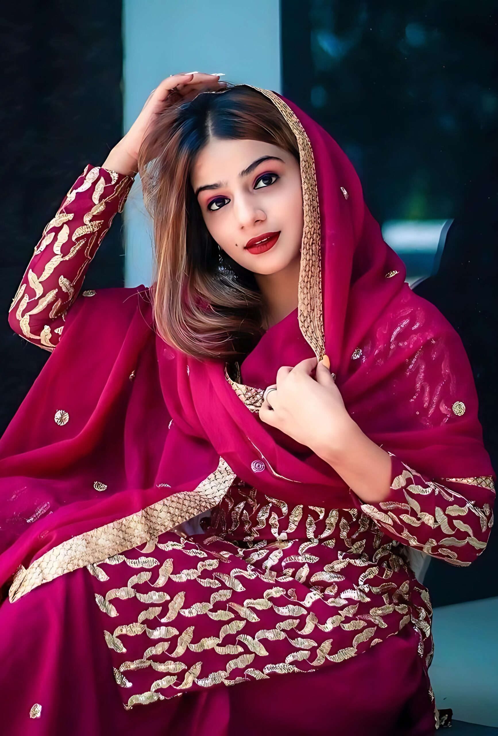 Modern Muslim girl in maroon traditional dress with golden embroidery, posing confidently with soft makeup and open hair
