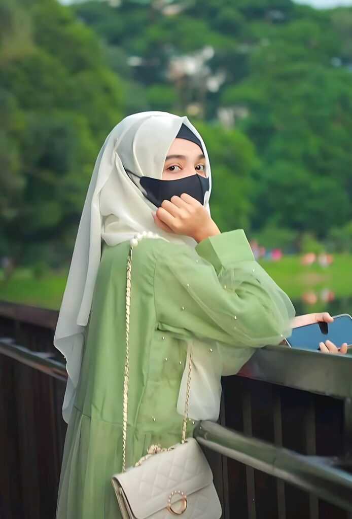 Elegant hijab girl wearing a green dress and white headscarf standing on a bridge holding a phone – full HD profile picture.