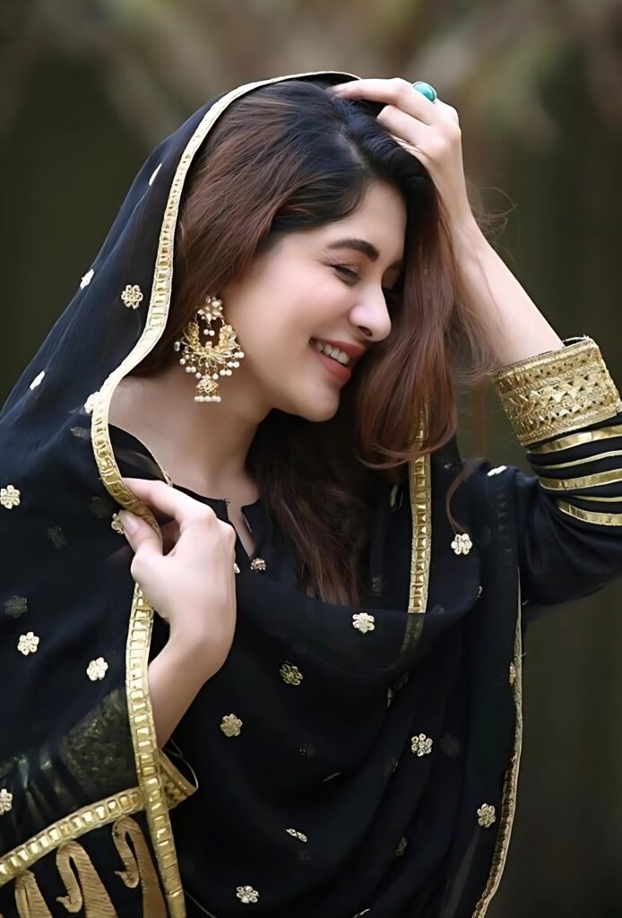 Muslim girl in black traditional dress with golden embroidery, smiling while adjusting her dupatta, perfect for display picture