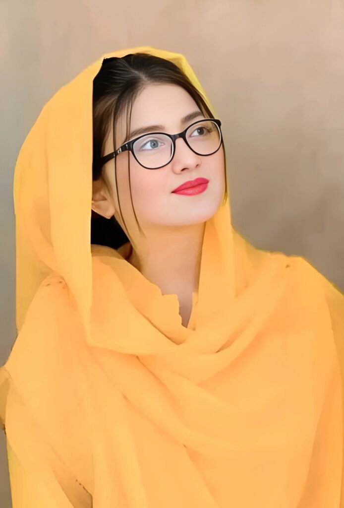 Young Muslim girl in a bright yellow dupatta with glasses and red lipstick looking upwards thoughtfully