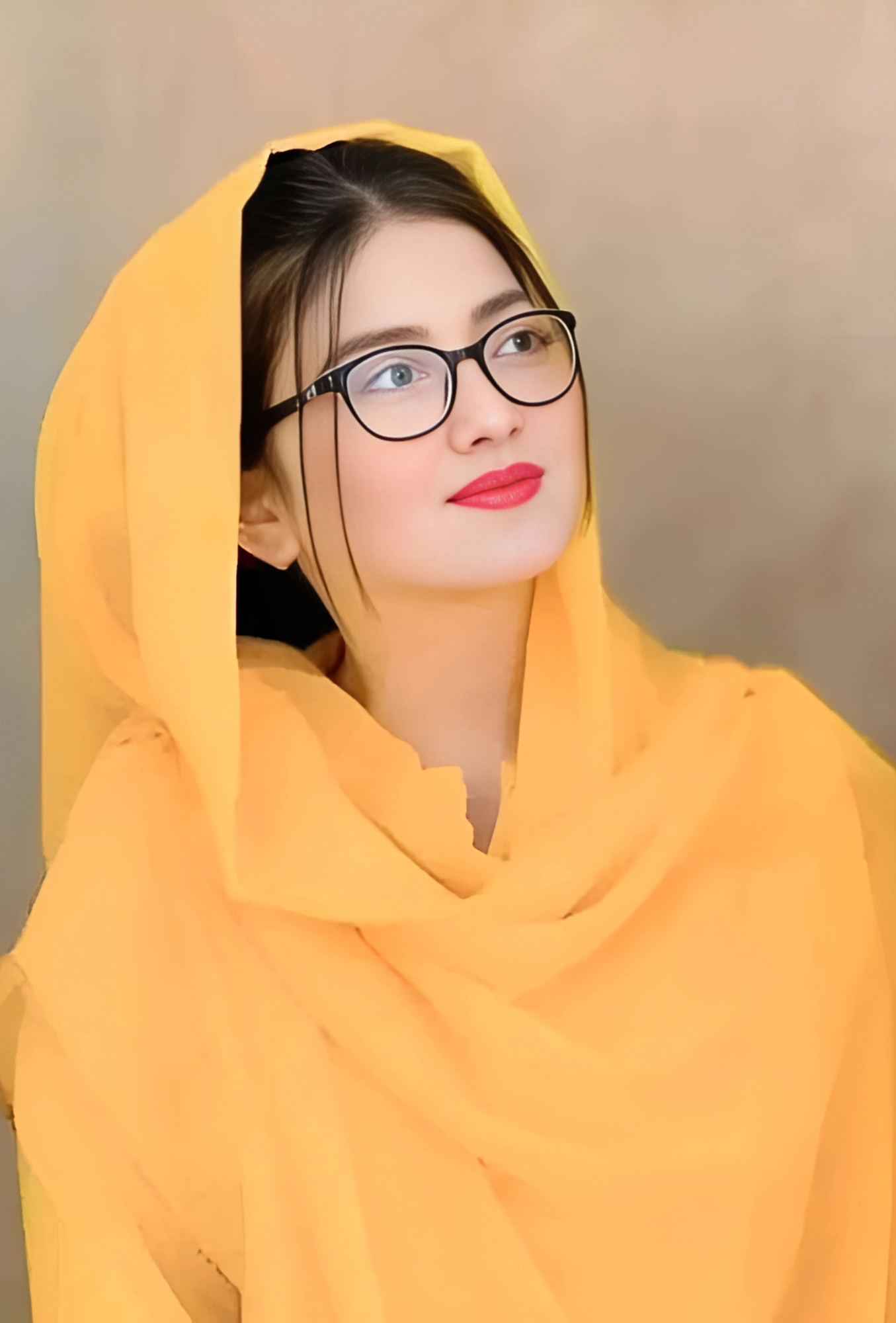 Young Muslim girl in a bright yellow dupatta with glasses and red lipstick looking upwards thoughtfully
