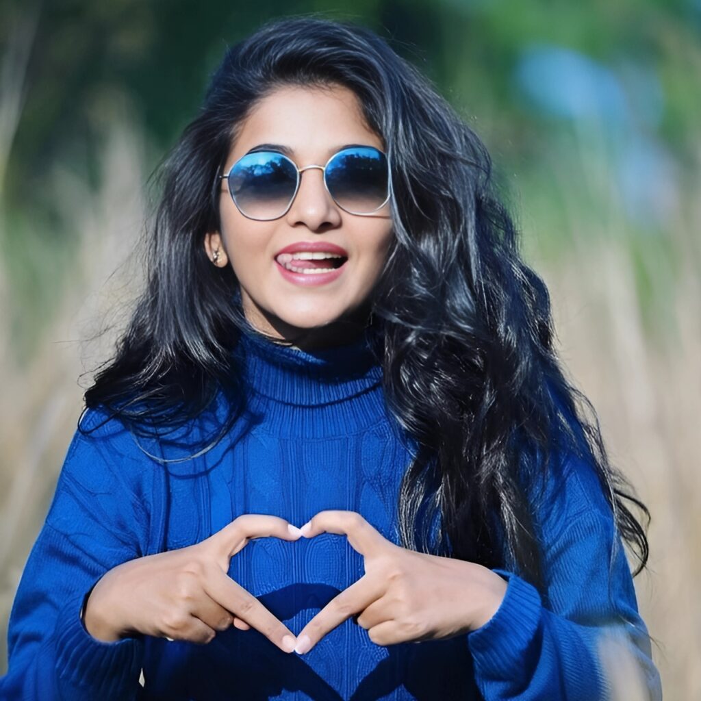 Girl in blue sweater showing heart sign with hands, wearing sunglasses, smiling with tongue out – stylish outdoor pose for WhatsApp DP